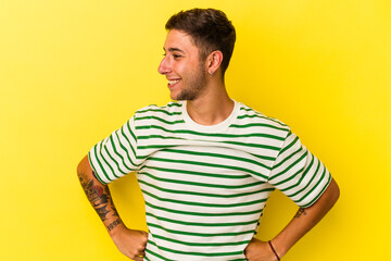 Young caucasian man with tattoos isolated on yellow background  laughs happily and has fun keeping...