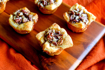 Pecan Pie Tartelettes Served on a Wooden Cutting Board: Individual pecan pie tarts displayed on a...