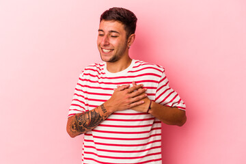 Young caucasian man with tattoos isolated on yellow background  has friendly expression, pressing palm to chest. Love concept.