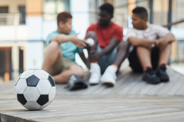Focus on soccer ball on wooden podium outdoors, black father talking to sons in background
