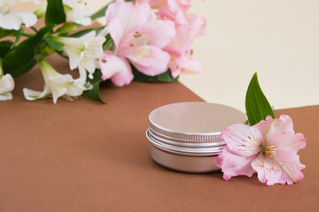 Obraz na płótnie Canvas aluminum cosmetic cream jar and beautiful pink and white lily flowers on beige brown background