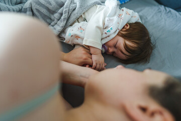 Obraz na płótnie Canvas Mother caucasian woman hold hand of baby daughter while sleeping on the bed at home in day