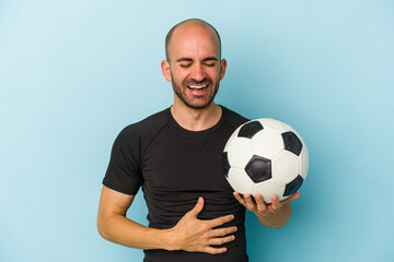 Young business bald man playing football isolated on blue background  laughing and having fun.