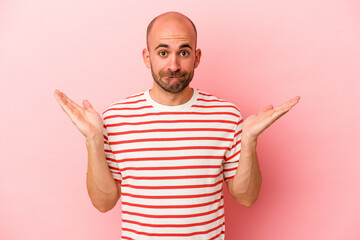Young caucasian bald man isolated on pink background  confused and doubtful shrugging shoulders to hold a copy space.