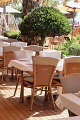 Wicker tables and chairs on an outside terrace of a restaurant on a sunny day.