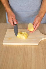 close up of a man cutting a peeled potato in dices on a wood cutting board