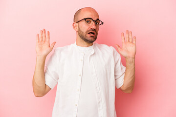 Young caucasian bald man isolated on pink background  being shocked due to an imminent danger
