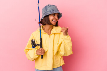 Young mixed race woman practicing fishing isolated on pink background points with thumb finger away, laughing and carefree.