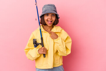 Young mixed race woman practicing fishing isolated on pink background smiling and pointing aside, showing something at blank space.