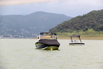 Motorboats, yachts and sailboats sailing on the lake surrounded by mountains full of green trees
