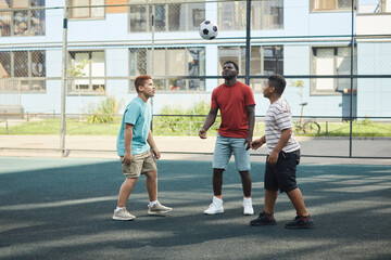 Group of black boys standing in circle and looking at ball while playing soccer at playground
