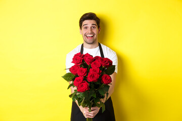 Seller in flower shop wearing black apron, giving bouquet of roses and smiling, standing over...