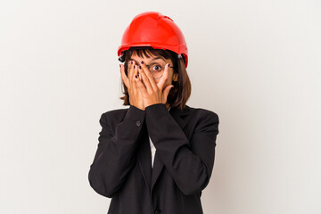 Young architect woman with red helmet isolated on white background blink through fingers frightened and nervous.