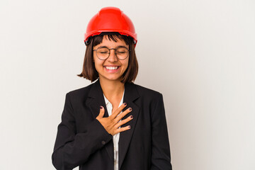 Young architect woman with red helmet isolated on white background laughs out loudly keeping hand on chest.