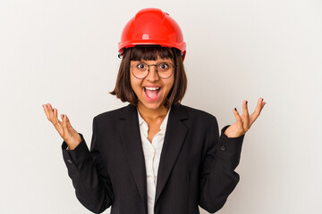 Young architect woman with red helmet isolated on white background receiving a pleasant surprise, excited and raising hands.