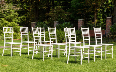 Empty white chairs spread out on the green grass, outdoors.