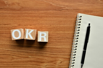 On a wood board, wooden word cubes are arranged in the letters OKR. It is an abbreviation for Objectives Key Results.