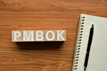 On a wood board, wooden word cubes are arranged in the letters PMBOK. It is an abbreviation for Project Management Body of Knowledge.