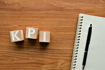 On a wood board, wooden word cubes are arranged in the letters KPI. It is an abbreviation for Key...