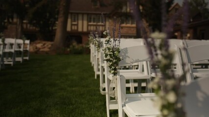 Dolly back, rack focus, beautiful flowers at exterior wedding with white chairs.