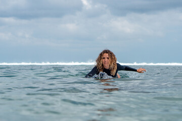 Portrait of surfer girl on white surf board in blue ocean pictured from the water