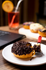 Chocolate Meses Doughnut on white plate with laptop as background and a glass of fruit syrup