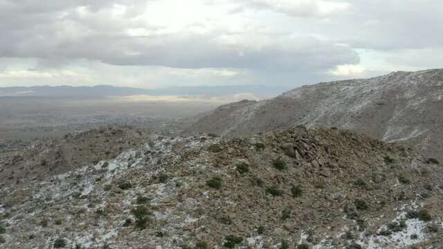 Snowfall on the hills of Joshua Tree National Park with storm clouds in background.