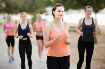 Positive girls running during outdoor workout on city seafront.