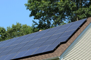 Solar panels on top of a house roof on a sunny summer day with blue sky and trees in the background