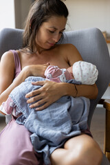 Mother breastfeeds newborn baby while sitting in chair