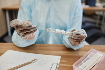 Hands of physician in PPE suit putting swab with nose mucus of patient in test tube to send to...