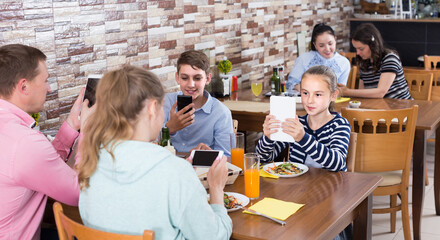 Obraz premium Modern family busying with phone during lunch in family cafe.