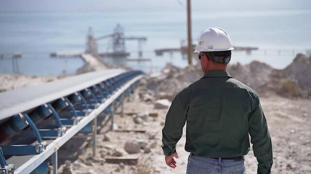 Worker inspects conveyor belt transporting plaster to the port in background.