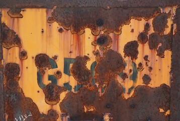 Discarded metal panel with flaking yellow paint and stenciled numbers obliterated by rust and holes