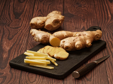 Ginger root cut into strips and slices on a burned wood cutting board over a brown wood background, shallow focus