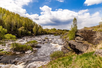 Summer landscape with fast-flowing river, stone banks, trees and blue sky with white clouds