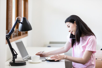 Asian young woman in pink shirt working on her laptop computer while sitting in living room at home.