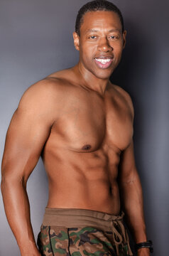 Portrait of shirtless, muscular Black man standing in front of gray wall