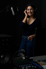 Beautiful Asian woman as elegant singer wearing acoustic headphone happy on pretty voice and enjoy sweet melody performing by beautiful song singing to mic in dark sound record room of music studio.