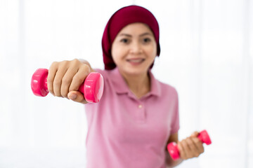 Cutout of pink plastic dumbbell grabbed by hands of cheerful Asian woman patient of breast cancer...