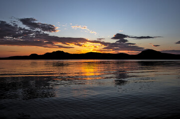 朝焼けの空を僅かに波打った湖面に映す湖。日本の北海道の屈斜路湖で。