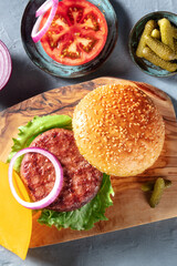 Hamburger recipe. Classic meat burger ingredients with a beef patty, sesame buns, tomato, onion, salad leaf and pickles, shot from the top