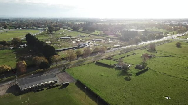 Drone dropdown shot, flying over filed towards the motorway with cars, grass, and trees in the residential area in Cambridge New Zealand