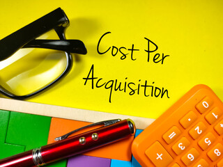 Business concept.Text Cost Per Acquisition with calculator,glasses,pen and wooden puzzle on yellow...