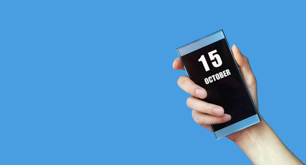 october 15. 15th day of the month, calendar date.Woman's hand holds mobile phone with blank screen on blue isolated background.Autumn month, day of the year concept
