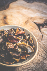 Rustic concept of dried boletus edulis in a ceramic bowl. Kitchen tool on natural wooden background. Selective focus on sliced food, blurred background.