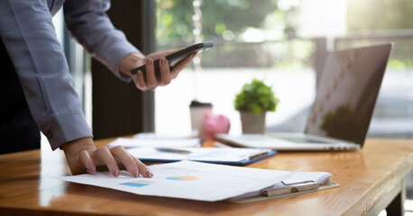 Business woman discussing on stockmarket charts in office, working on smart phone and laptop computer