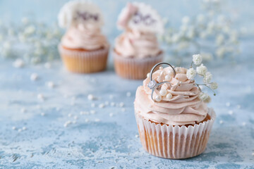 Tasty cupcake and wedding rings on table