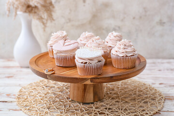 Dessert stand with tasty cupcakes and wedding rings on table