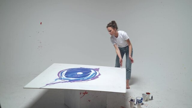 Experimental painting, young female artist draws by pouring paint and rotating the canvas, a talented artist draws a color blue abstraction.